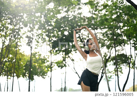 Beautiful young African woman wearing headphones practicing yoga on mat in a park Beautiful young African woman wearing headphones practicing yoga on mat in a park 121596005