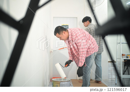 Two young asian men painting walls with a roller brush during renovation 121596017