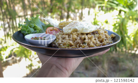 A hand holding or carry a plate of fried rice with nature background. A hand holding or carry a plate of fried rice with nature background. 121598142
