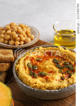 close up Homemade pumpkin chickpea hummus in a bowl on wooden board on light background. copy space close up Homemade pumpkin chickpea hummus in a bowl on wooden board on light background. copy space 121599784