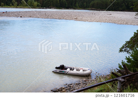Inflatable boat moored on a serene riverbank with forest backdrop. 121601716