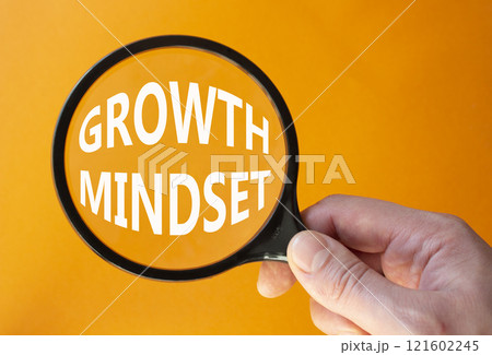 Growth Mindset symbol. Concept word Growth Mindset on magnifying glass. Beautiful orange background. Businessman hand. Business and Growth Mindset concept. Copy space 121602245