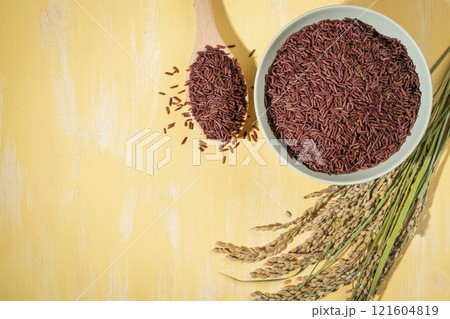 A bowl of red-rice is placed on a table next to a wood spoonful and ears of rice A bowl of red-rice is placed on a table next to a wood spoonful and ears of rice 121604819