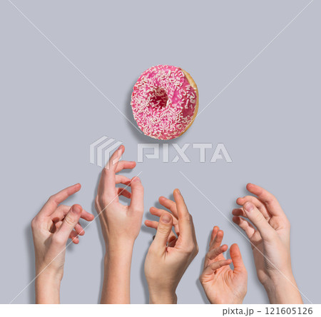 Several hands reach for a levitating  glazed pink donut on blue background. Several hands reach for a levitating  glazed pink donut on blue background. 121605126
