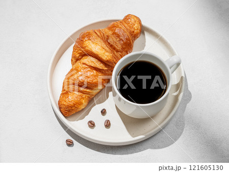 Cup of freshly brewed espresso coffee and fresh croissant on white plate on light background Cup of freshly brewed espresso coffee and fresh croissant on white plate on light background 121605130