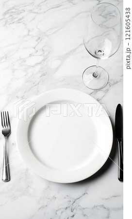 Blank ceramic plate on a marble table with silver cutlery and a wine glass setting for dining 121605438