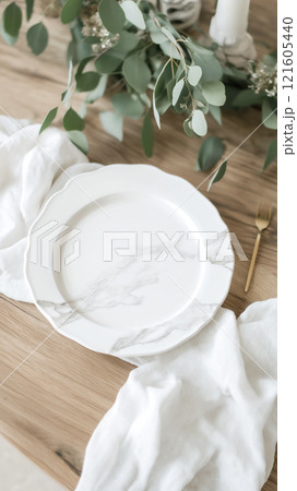 Blank ceramic plate placed on a rustic wooden table with greenery and linen cloth 121605440