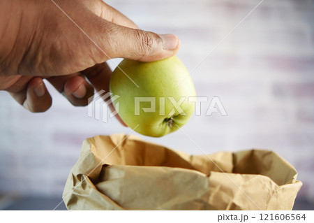A hand is holding a fresh green apple above a brown paper grocery bag A hand is holding a fresh green apple above a brown paper grocery bag 121606564