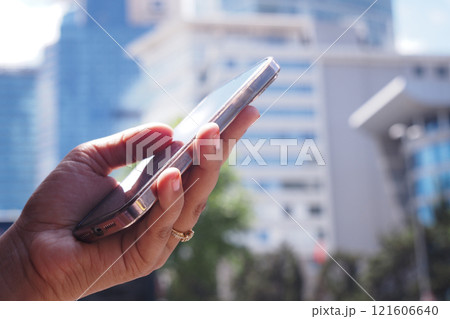 Individual with a smartphone amidst an urban landscape background 121606640