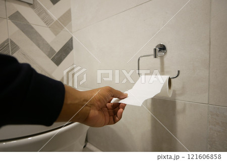 Hand pulling toilet paper roll in holder 121606858