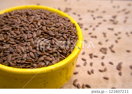 Close-Up Shot of Flaxseeds, Linseeds in a Yellow Bowl with Seeds Spread on a Wooden Table 121607211