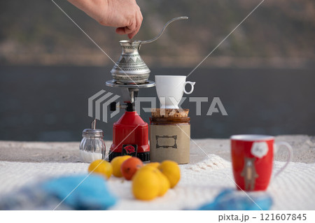 Brewing coffee by the water at sunset with a scenic view of Montenegro and fresh fruit on a cozy table, creating a relaxing atmosphere for enjoyment and reflection on a peaceful day Brewing coffee by the water at sunset with a scenic view of Montenegro and fresh fruit on a cozy table, creating a relaxing atmosphere for enjoyment and reflection on a peaceful day 121607845