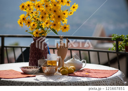 Bright yellow flowers in a vase on a table set with colorful dishes and a scenic backdrop creates a warm atmosphere for morning tea on a sunny day Bright yellow flowers in a vase on a table set with colorful dishes and a scenic backdrop creates a warm atmosphere for morning tea on a sunny day 121607851