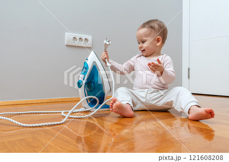 Little one captivated by household appliance cord, presenting a hidden hazard in plain sight. 121608208