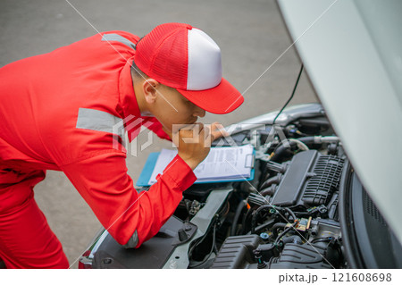 Automobile Mechanic Inspecting Engine with Service Report on Clipboard 121608698