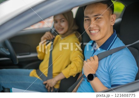 A Young Couple Smiling Happily in a Car with Seatbelts Fastened for Safety 121608775