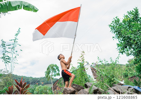 shirtless child standing waving the Indonesian flag with nature in the background 121608865