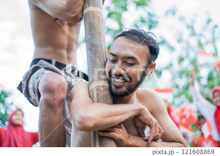 smiling bearded man embracing a pole participating in a areca climbing competition smiling bearded man embracing a pole participating in a areca climbing competition 121608869