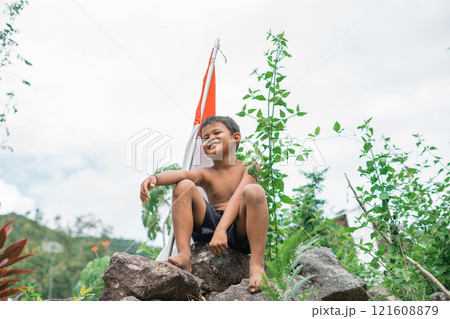 boy sitting on rock with stick with Indonesian flag on nature background boy sitting on rock with stick with Indonesian flag on nature background 121608879