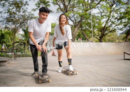 Two close friends are having a great time skateboarding together at a sunny skate park 121608944