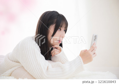 うつ伏せで寝転がりスマホを見る検索、タップする若い女性のクローズアップ うつ伏せで寝転がりスマホを見る検索、タップする若い女性のクローズアップ 121610843