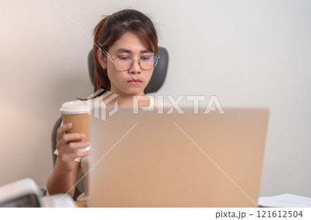 Stressed Asian woman drinking Coffee while working, female businesswoman using laptop with tired and sleepy at office, Exhausted woman with computer at home late night. Overload and Overworked 121612504