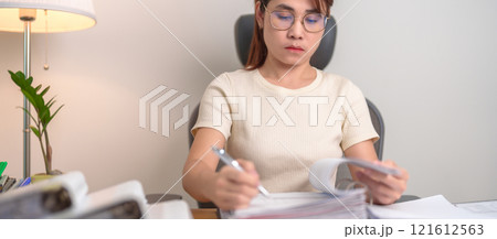 Asian woman reading financial report, female businesswoman sign contract or writing documents paper at home or office late night. Overworked, work hard and business concept Asian woman reading financial report, female businesswoman sign contract or writing documents paper at home or office late night. Overworked, work hard and business concept 121612563