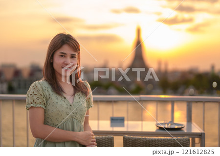 tourist woman enjoys view to Wat Arun Temple in sunset, Traveler visits Temple of Dawn near Chao Phraya river from rooftop bar. Landmark and Travel destination in Bangkok, Thailand and Southeast Asia 121612825
