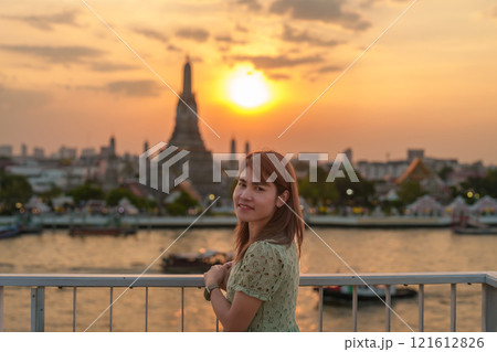 tourist woman enjoys view to Wat Arun Temple in sunset, Traveler visits Temple of Dawn near Chao Phraya river from rooftop bar. Landmark and Travel destination in Bangkok, Thailand and Southeast Asia 121612826