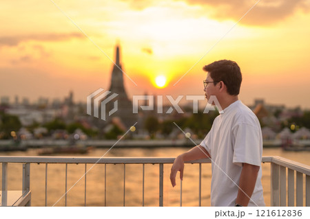 tourist man enjoys view to Wat Arun Temple in sunset, Traveler visits Temple of Dawn near Chao Phraya river from rooftop bar. Landmark and Travel destination in Bangkok, Thailand and Southeast Asia 121612836