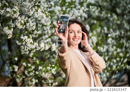 Happy woman taking selfie with smartphone among spring blossoms with soft focus on the background. Happy woman taking selfie with smartphone among spring blossoms with soft focus on the background. 121615147