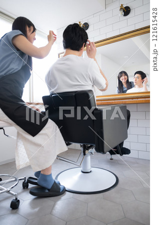 美容室の鏡の前で髪の毛の確認やカウンセリングをする女性美容師と男性客 縦長 美容室の鏡の前で髪の毛の確認やカウンセリングをする女性美容師と男性客 縦長 121615428