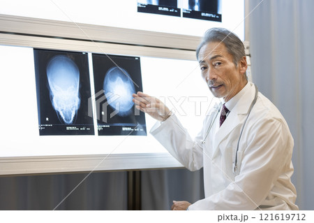 頭部のレントゲン写真を見ながら説明するベテランの医師 頭部のレントゲン写真を見ながら説明するベテランの医師 121619712