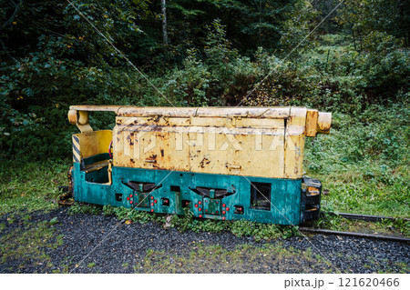 An abandoned mining locomotive sits peacefully among overgrown vegetation, showcasing its weathered body and colorful paint. This relic of industry contrasts with the surrounding forest. An abandoned mining locomotive sits peacefully among overgrown vegetation, showcasing its weathered body and colorful paint. This relic of industry contrasts with the surrounding forest. 121620466