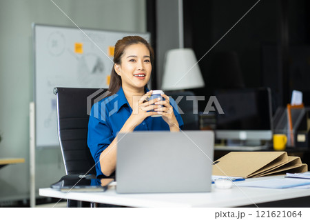 Asian businesswoman sits in a office working and enjoys a coffee. Asian businesswoman sits in a office working and enjoys a coffee. 121621064