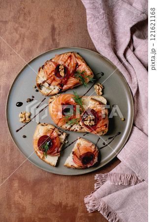 Sandwiches with thinly sliced salted salmon fillet, beetroot slices, walnuts, balsamic vinegar and fresh wheat bread on grey plate, fine dining. Brown background, top view. Colors of the year 2025. Sandwiches with thinly sliced salted salmon fillet, beetroot slices, walnuts, balsamic vinegar and fresh wheat bread on grey plate, fine dining. Brown background, top view. Colors of the year 2025. 121621168