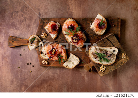 Sandwiches with thinly sliced salted salmon fillet, sardines, beetroot slices, walnuts, balsamic vinegar and fresh wheat bread on wooden board. Brown background, top view. Colors of the year 2025. Sandwiches with thinly sliced salted salmon fillet, sardines, beetroot slices, walnuts, balsamic vinegar and fresh wheat bread on wooden board. Brown background, top view. Colors of the year 2025. 121621170
