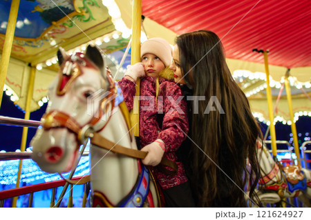 Joyful mother and daughter share a moment on a carousel at night Joyful mother and daughter share a moment on a carousel at night 121624927