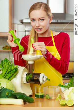 Woman in kitchen making vegetable smoothie juice 121625929