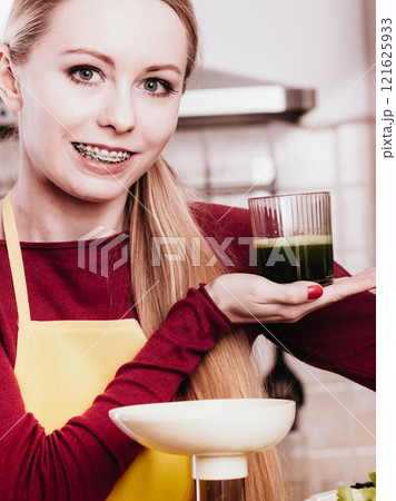 Woman in kitchen holding vegetable smoothie juice Woman in kitchen holding vegetable smoothie juice 121625933