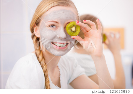Happy young woman having face mask holding kiwi Happy young woman having face mask holding kiwi 121625959