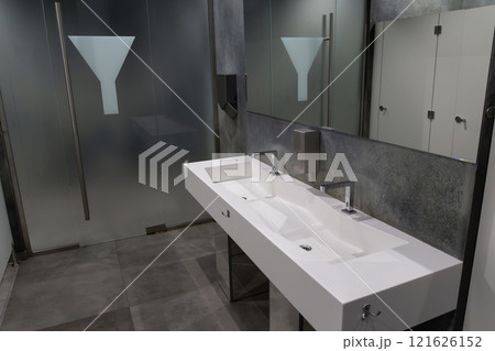 A spacious bathroom showcases a sleek, modern sink with dual faucets and a minimalist aesthetic. Frosted glass partitions add privacy, creating a contemporary atmosphere for users A spacious bathroom showcases a sleek, modern sink with dual faucets and a minimalist aesthetic. Frosted glass partitions add privacy, creating a contemporary atmosphere for users 121626152