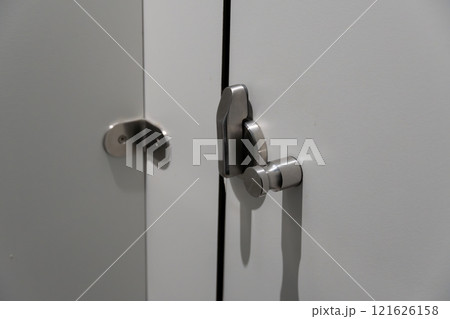 A pair of sleek stainless steel locks are fastened to a white cabinet door, highlighting the modern design elements of the interior space 121626158