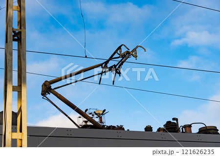 Overhead lines and pantographs exhibit the advanced electric train system, highlighting the industrial architecture of modern rail transportation against a vibrant blue sky 121626235