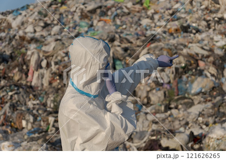 A sanitation worker in protective clothing gestures towards an expansive landfill brimming with plastic waste and debris A sanitation worker in protective clothing gestures towards an expansive landfill brimming with plastic waste and debris 121626265