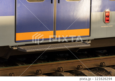 Close-up of a modern electric train door positioned at a railway station. The vibrant colors contrast with the rail tracks and surrounding environment during sunset, creating a striking visual Close-up of a modern electric train door positioned at a railway station. The vibrant colors contrast with the rail tracks and surrounding environment during sunset, creating a striking visual 121626294