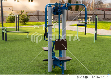 A piece of fitness training equipment stands ready for use in an outdoor gym, surrounded by green grass and other exercise areas, providing a healthy lifestyle option for the community A piece of fitness training equipment stands ready for use in an outdoor gym, surrounded by green grass and other exercise areas, providing a healthy lifestyle option for the community 121626302