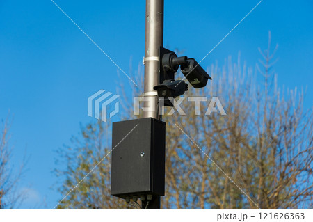CCTV cameras are securely mounted on metal poles, actively monitoring the surroundings in an outdoor area surrounded by trees, during clear blue sky daylight conditions 121626363