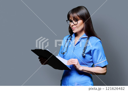 Portrait of female nurse with clipboards, on grey studio background 121626482