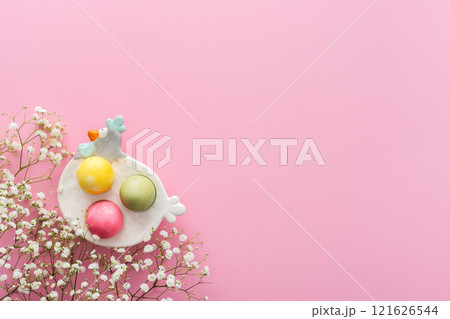 Easter eggs in a decorative hen with gypsophila flowers on a pink background 121626544